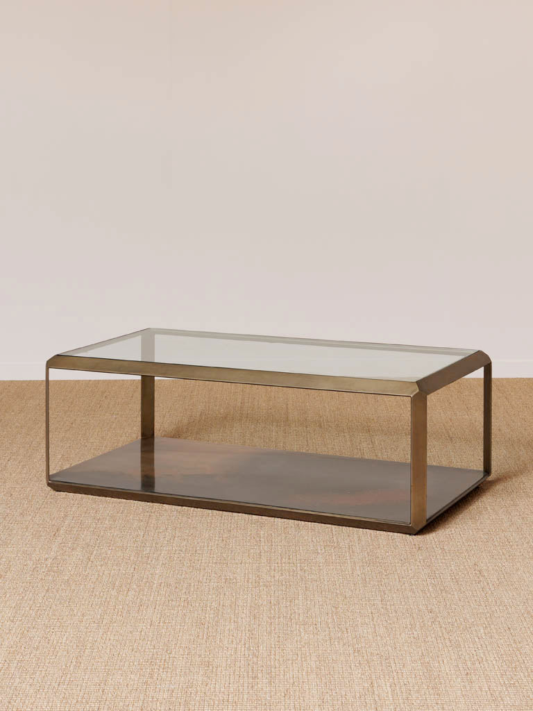 Couchtisch Baptiste neben Sofa, dekoriert mit Kerzen und Kunstblumen. Der braune Eisen- und Glas-Tisch ergänzt deine Wohnzimmerdekoration mit einem Hauch von Kunst und Eleganz